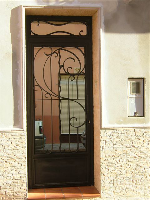 Puerta de una hoja con fijo en parte superior adornos trabajados con la fragua de una manera artesanal. Diseño personalizado.Trabajo laborioso y artesanal bien ejecutado.