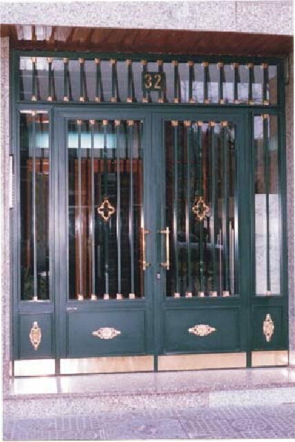 Puerta lisa con fijos laterales barrotes con macollas doradas y plancha decorada.